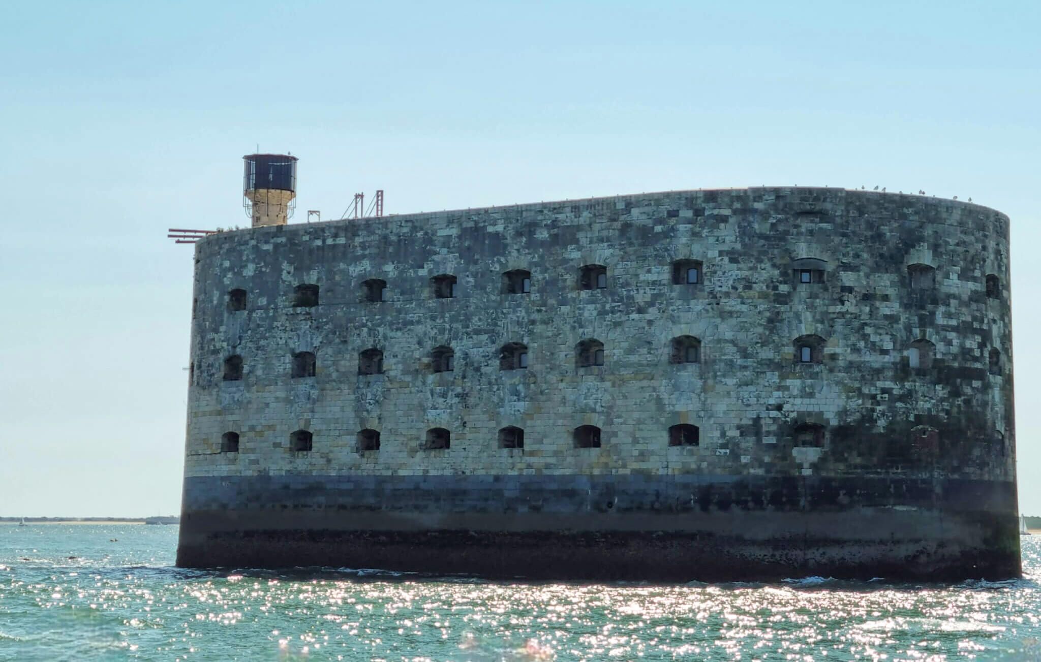 A large, historic stone building with multiple arched windows, situated by a body of water.