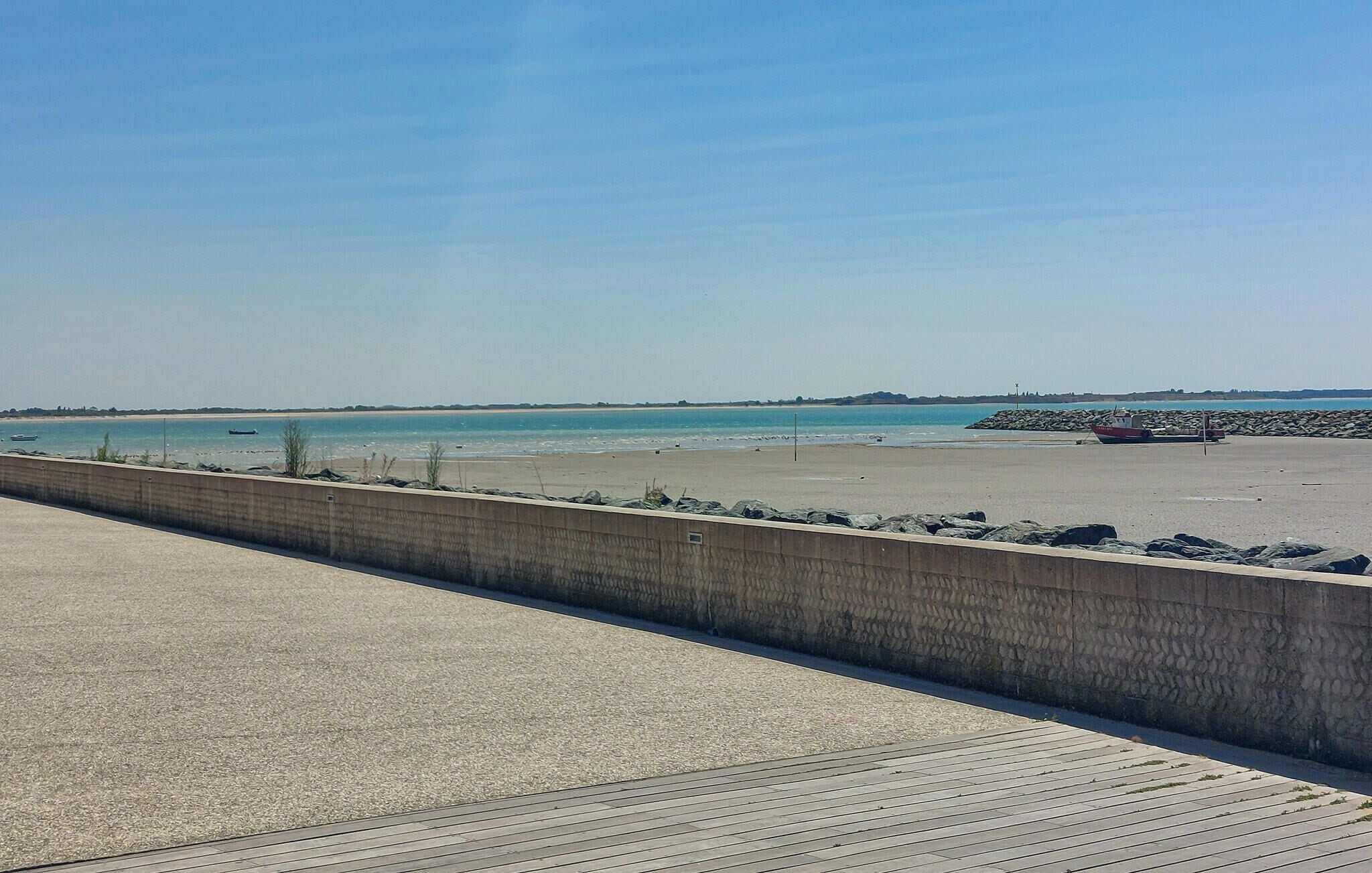 A coastal walkway with a concrete barrier, a sandy beach, and a rocky breakwater.
