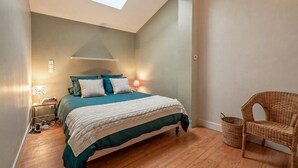 Ein Schlafzimmer mit Bett, Nachttischlampen, einem Korbstuhl und einem Dachfenster.