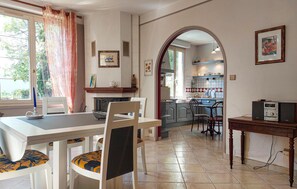 A dining area with a table and chairs, a kitchen with a tiled backsplash, and a doorway leading to another room. - Charmante maison proche plage (Châtelaillon-Plage)