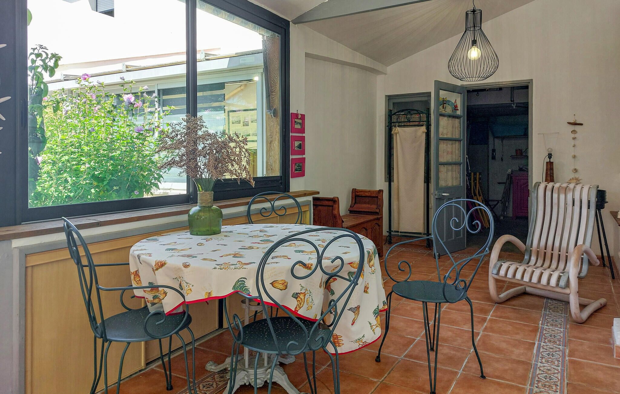 Een eetruimte met een tafel gedekt voor vier personen, omringd door stoelen, een vaas met bloemen en een uitzicht door een raam.