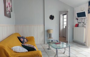 Un salon avec un canapé jaune, une table basse en verre, une lampe et une horloge murale.