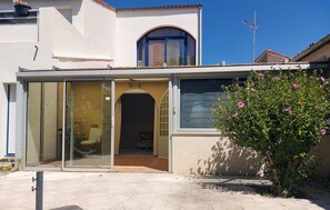 Une maison avec une porte d’entrée en verre, un petit porche et un arbuste à fleurs.
