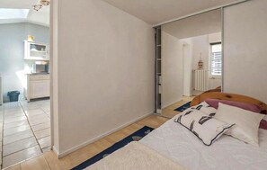 A bedroom with a bed, a wardrobe, a mirror, and a kitchenette in the background. - Charmante maison proche plage (Châtelaillon-Plage)