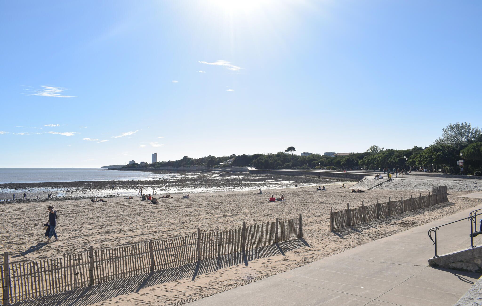 Une plage avec une clôture en bois, une promenade en béton et un ciel dégagé.