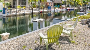 A tranquil pool area with a thatched-roof hut, surrounded by palm trees and a pebbled walkway. - Waterfront Escape - Canal Front, 50ft Dock, King Beds and Pet Friendly (Little Torch Key)