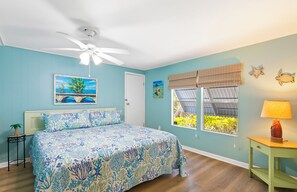A bedroom with a bed, a ceiling fan, a window with a view, and a nightstand with a lamp. - Waterfront Escape - Canal Front, 50ft Dock, King Beds and Pet Friendly (Little Torch Key)