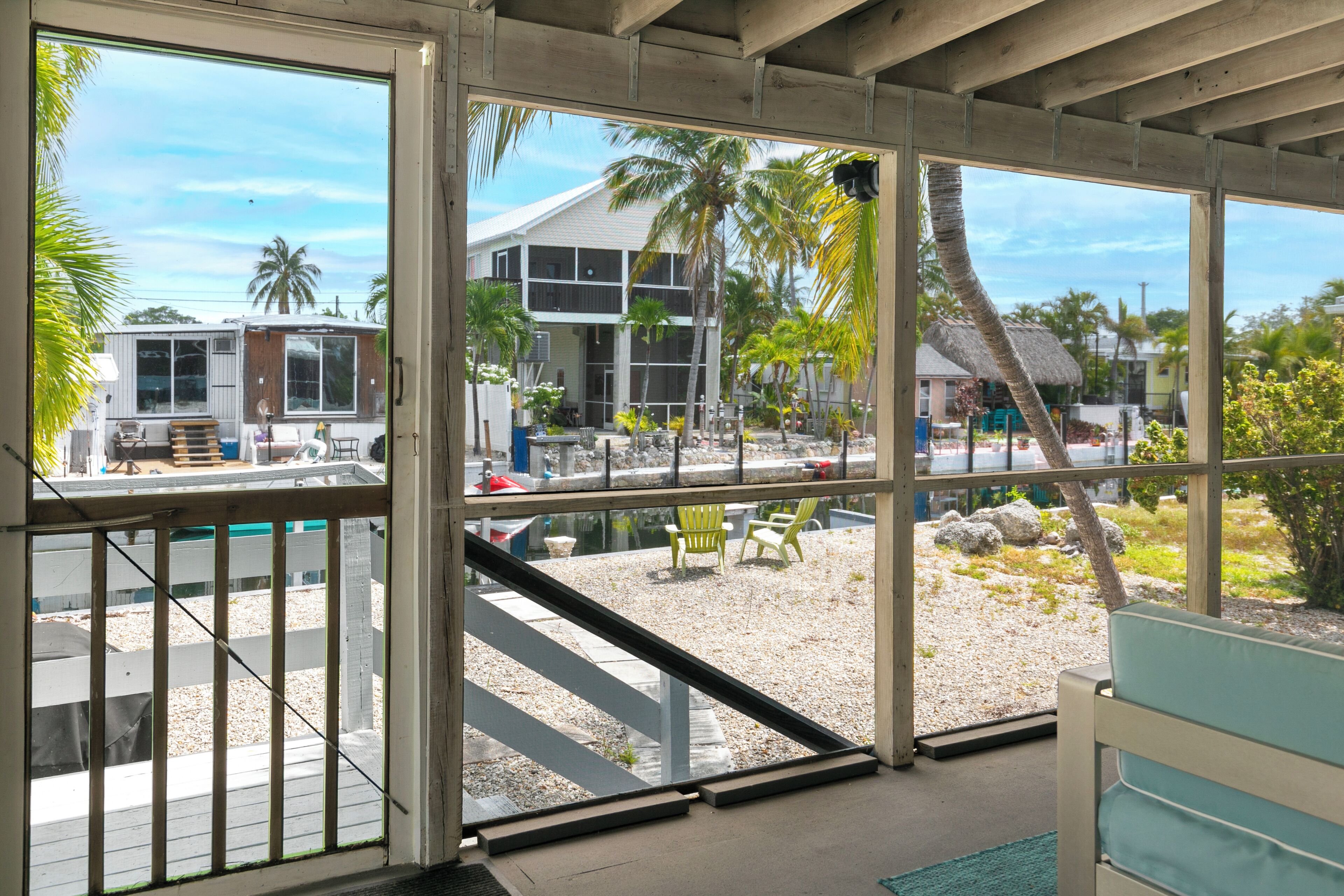 A view from inside a building with large windows overlooking a pool area, a building with a balcony, and palm trees.