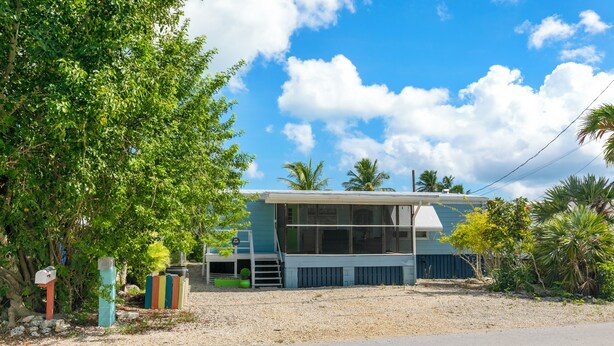 A two-story house with a balcony, surrounded by trees and a clear sky. - Waterfront Escape - Canal Front, 50ft Dock, King Beds and Pet Friendly (Little Torch Key)