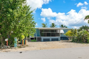 A two-story house with a balcony, surrounded by trees and a clear sky. - Waterfront Escape - Canal Front, 50ft Dock, King Beds and Pet Friendly (Little Torch Key)