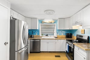 A compact kitchen with white cabinets, stainless steel appliances, a blue accent wall, and a fish decoration. - Waterfront Escape - Canal Front, 50ft Dock, King Beds and Pet Friendly (Little Torch Key)