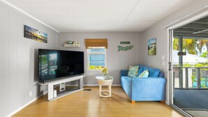 A living room with a flat-screen TV, a blue sofa, a small table with a vase, and a window with blinds. - Waterfront Escape - Canal Front, 50ft Dock, King Beds and Pet Friendly (Little Torch Key)