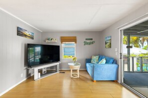 A living room with a flat-screen TV, a blue sofa, a small table with a vase, and a window with blinds. - Waterfront Escape - Canal Front, 50ft Dock, King Beds and Pet Friendly (Little Torch Key)