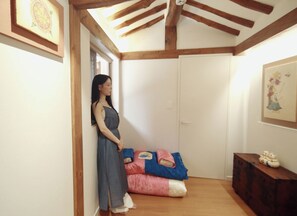 A room with a wooden ceiling, a bed with a pink and blue blanket, and a wooden dresser with a decorative item on top.