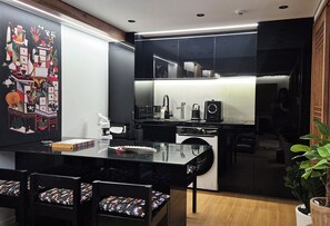 A modern kitchen with black cabinetry, a glass dining table, and a mural on the wall.
