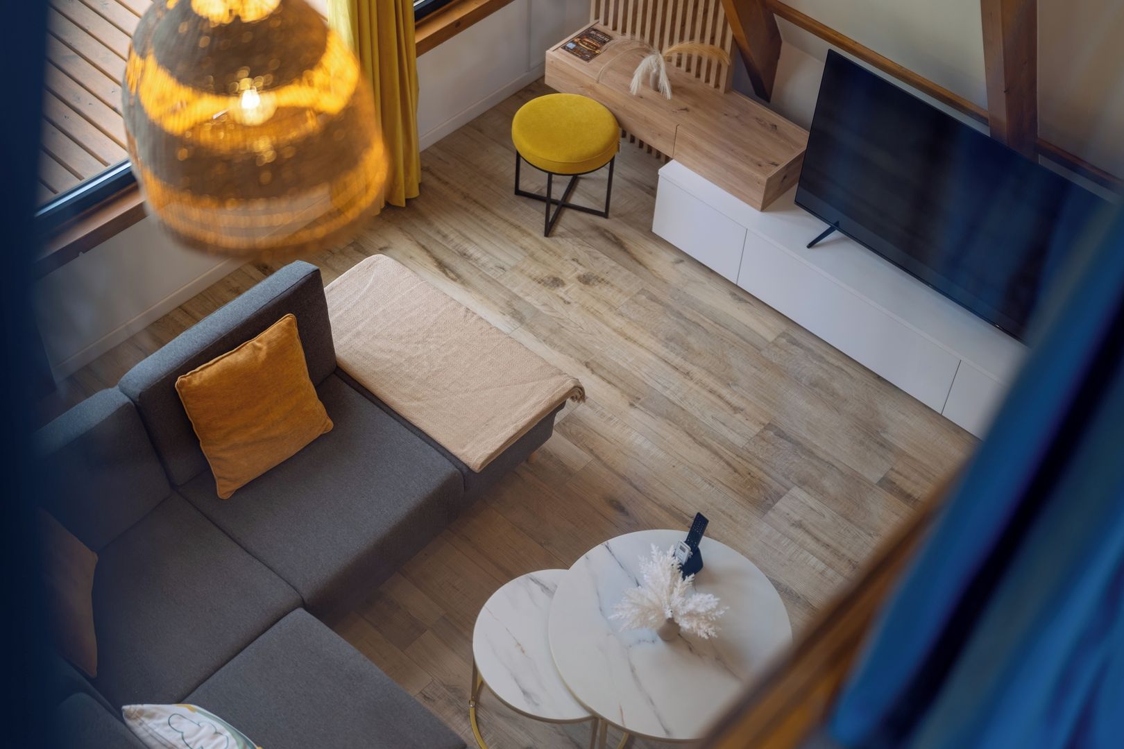 Een moderne woonkamer met een bank, poef en salontafel, houten vloeren en een televisie.