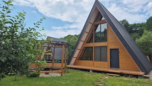 A modern A-frame wooden house with large windows and a deck.