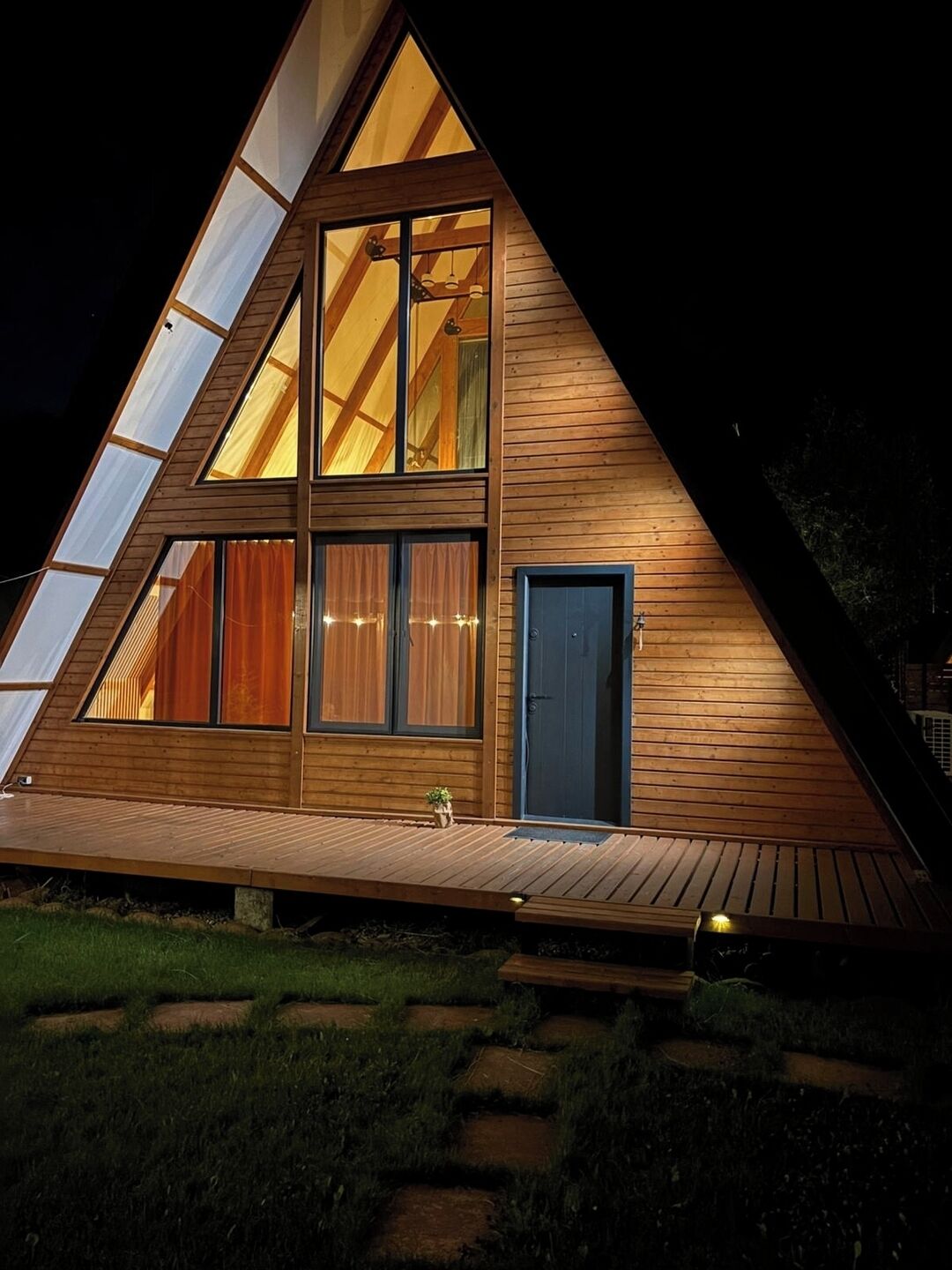 A modern, triangular wooden house with large windows and a visible door.
