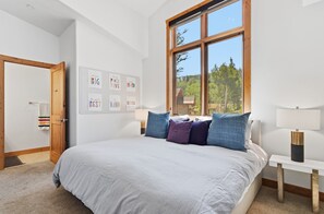 A bedroom with a large bed, a window with a view of trees, and motivational wall art.