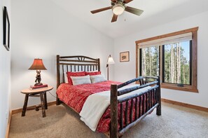 A bedroom with a wooden bed, two bedside lamps, a window with a view of trees, and a ceiling fan. - Rare 2 bedroom in The Colony! (Park City)