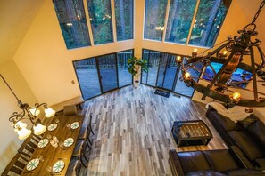 Ein geräumiges Zimmer mit hohen Decken, großen Fenstern, Holzboden, einem Esstisch mit Stühlen, einer Couch und einer Hängelampe.