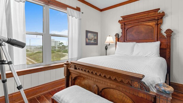Quarto com cama de madeira, um telescópio, janela com vista e uma luminária.
