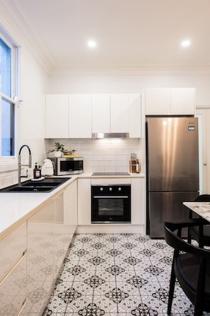 A modern kitchen with white cabinetry, a stainless steel refrigerator, a microwave, and a sink with a faucet. - Charming Family Home next to Westfields + Train (Woollahra)