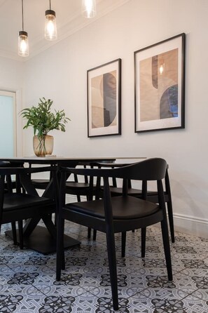 Et spiseområde med et bord, stole, en potteplante og to billeder hængende på væggen.