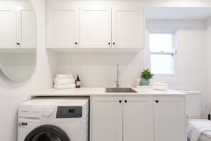 A compact laundry room with a washing machine, a sink, and cabinets. - Bondi Junction 4BR 2B Family Home + Secure Parking (Woollahra)