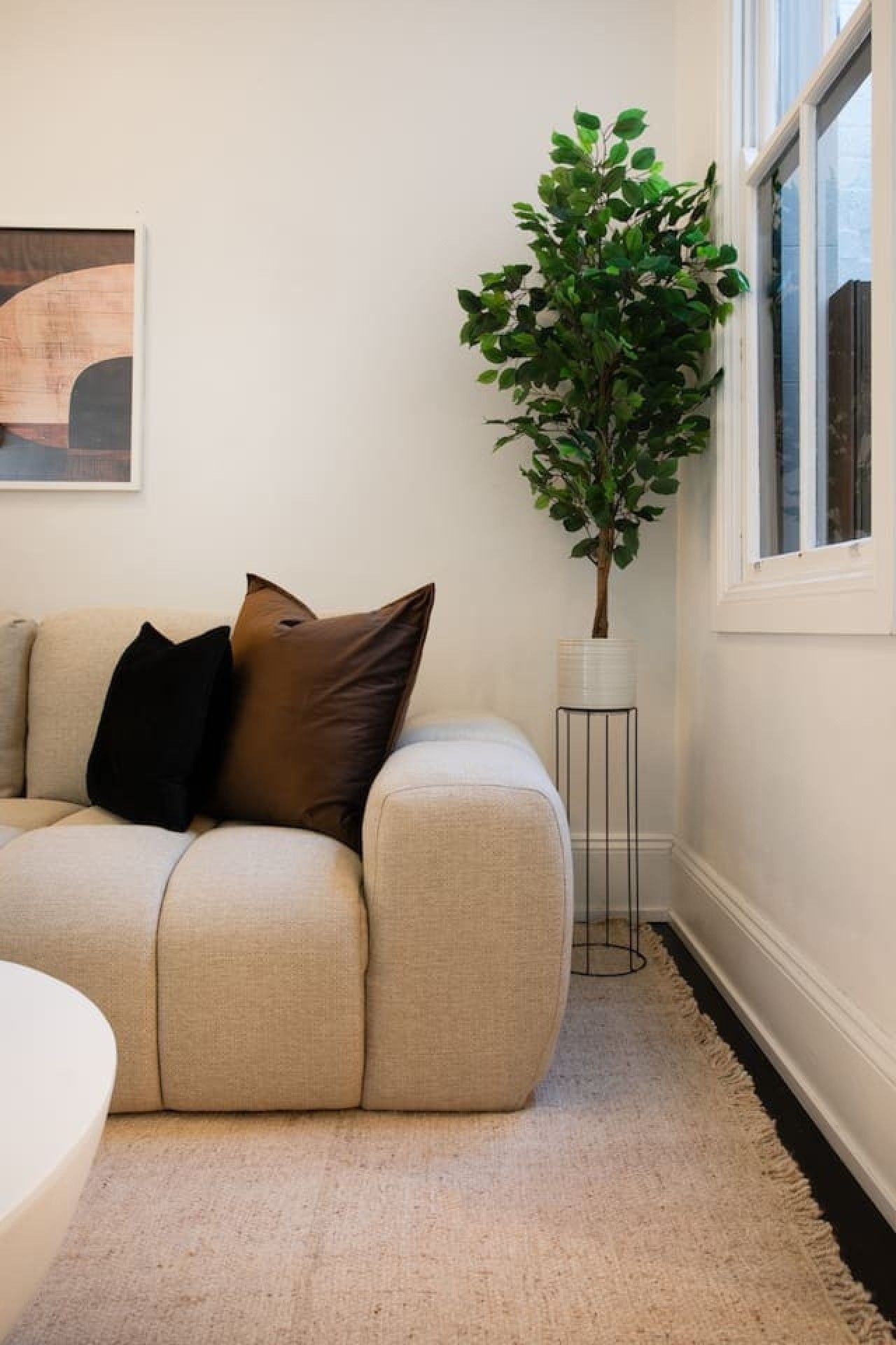 Un salon avec un canapé beige, une plante en pot et un tableau encadré accroché au mur.