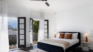 Ein Schlafzimmer mit Bett, Nachttischlampen, Deckenventilator und Blick durch offene Türen.