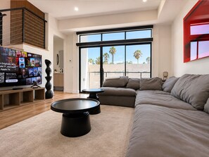 A modern living room with a large flat-screen TV, a sectional sofa, and a dining table. - All New Luxury 5-Level Home with Rooftop in the heart of LA, City Views, Parking (Los Angeles)