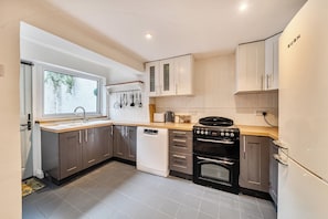 A modern kitchen with a dishwasher, stove, oven, and a window with a view of greenery. - Quaint Cottage in Charming Evesham (Evesham)