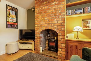 A living room with a brick fireplace, a television, a bookshelf, and a framed picture on the wall. - Quaint Cottage in Charming Evesham (Evesham)