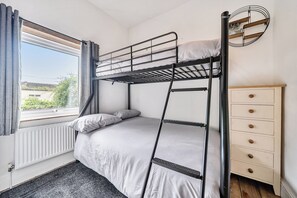 A bunk bed with a wooden ladder, a small dresser with drawers, a radiator, and a window with curtains. - Quaint Cottage in Charming Evesham (Evesham)