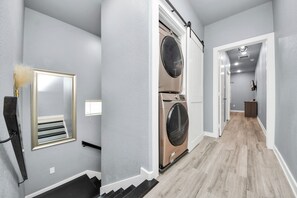 Un couloir donnant sur une buanderie avec une porte double, un miroir avec un cadre décoratif et un escalier avec une rampe noire.