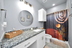Ein Badezimmer mit Granitplatte, einem runden Spiegel, einer Toilette und einer Duschvorhang mit Sonnendesign.