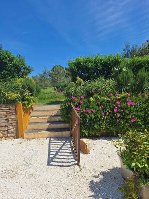 A gravel pathway leading to a wooden gate, surrounded by lush greenery and flowering plants. - Holiday home with swimming pool in a Mediterranean setting (Ližnjan)
