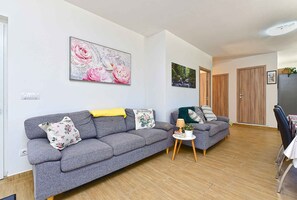 A modern living room with a grey sofa, a small side table, and a dining area with a chair and table. - Holiday home with swimming pool in a Mediterranean setting (Ližnjan)