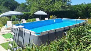 En rektangulær pool oven vands overflade med en stige på den ene side, omgivet af frodigt grønt og træer.