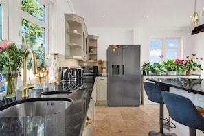 A modern kitchen with a stainless steel refrigerator, a double sink, and a bar area with a high chair. - Berry Lodge I 5 Bed House Sleeps 10 -Hot Tub -Spa (Upminster)