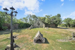 A stone structure resembling a small church or chapel with a grassy yard, a wooden fence, and a street lamp. - Berry Lodge I 5 Bed House Sleeps 10 -Hot Tub -Spa (Upminster)