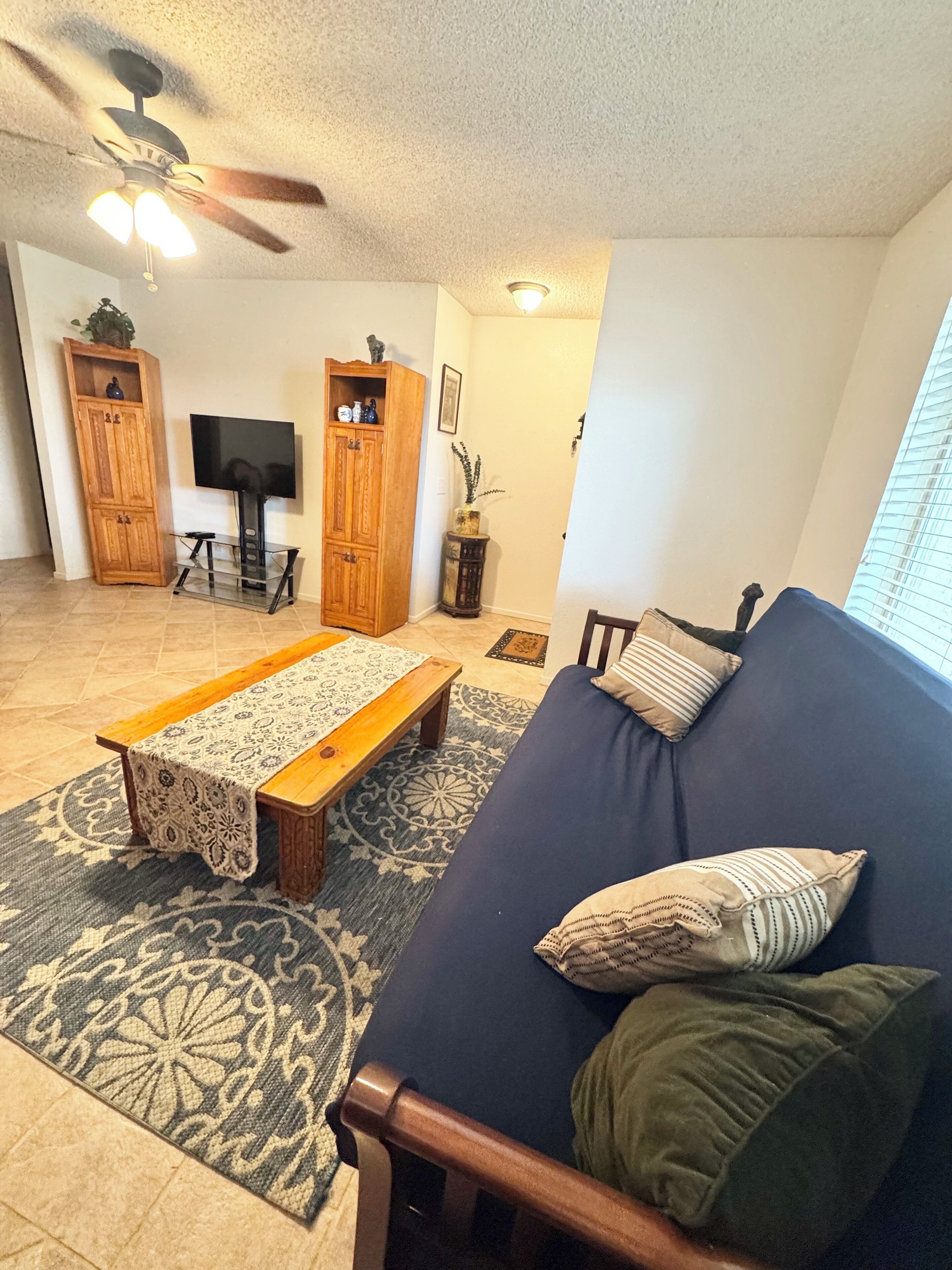 A living room with a sofa, a coffee table, a television, wooden cabinets, and a ceiling fan.