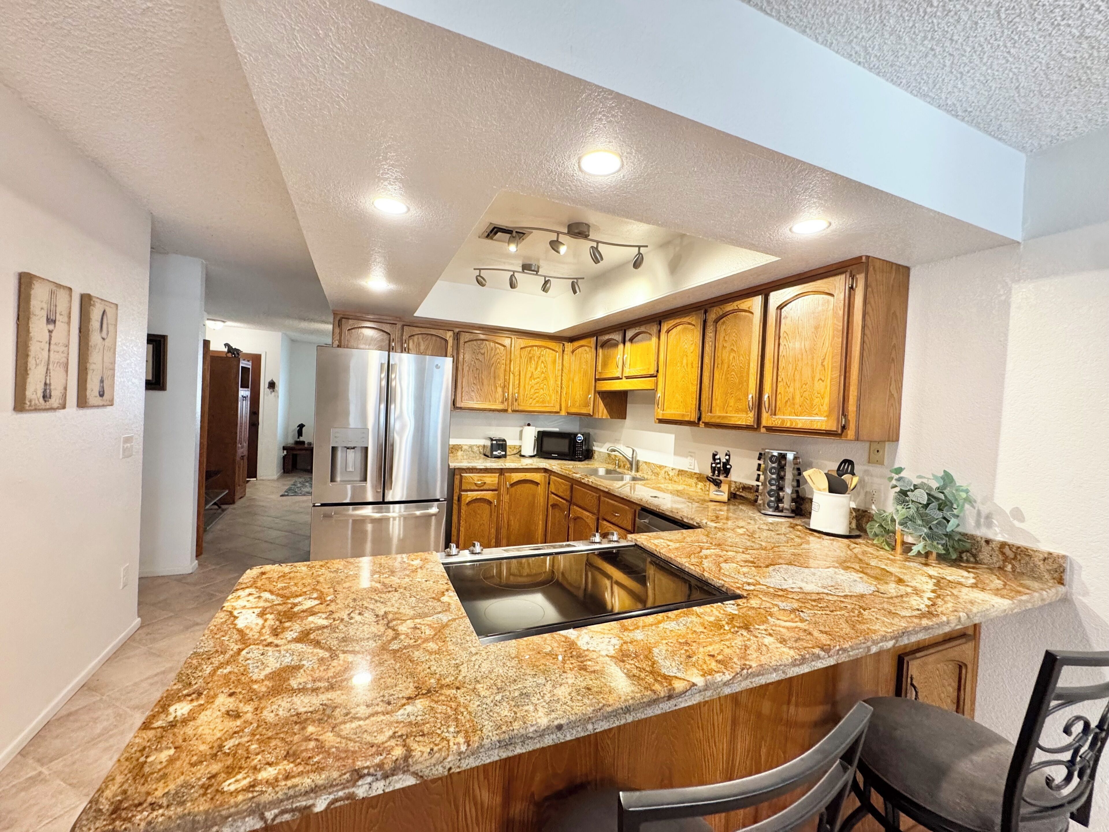 A modern kitchen with granite countertops, stainless steel appliances, wooden cabinets, and a central island with seating.