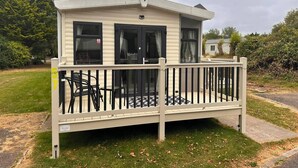 A single-story mobile home with a balcony, a small deck, and a visible number '57' on the side. - Homely Caravan in Skegness - Sleeps 6 (Skegness)