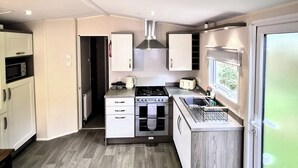 A compact kitchen with a built-in oven, microwave, and a small dining area. - Homely Caravan in Skegness - Sleeps 6 (Skegness)