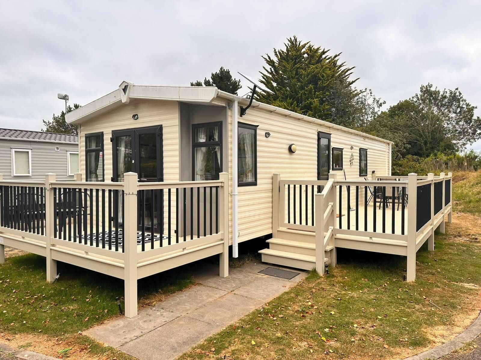 A mobile home with a deck and a small porch, surrounded by grass and trees.