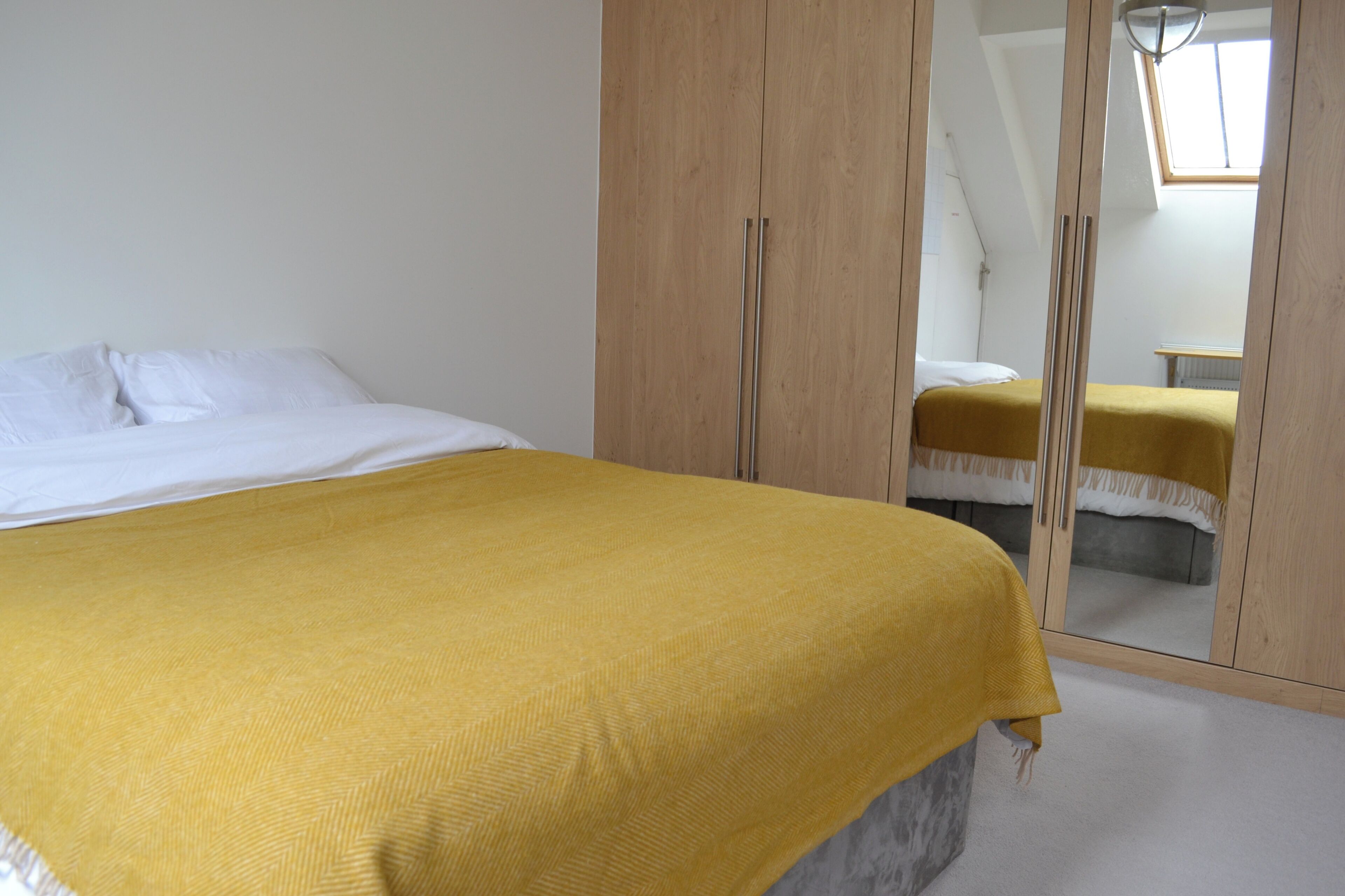 A bedroom with a bed, a wardrobe, and a mirror reflecting another bed.