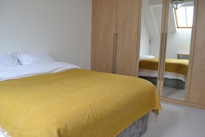 A bedroom with a bed, a wardrobe, and a mirror reflecting another bed.