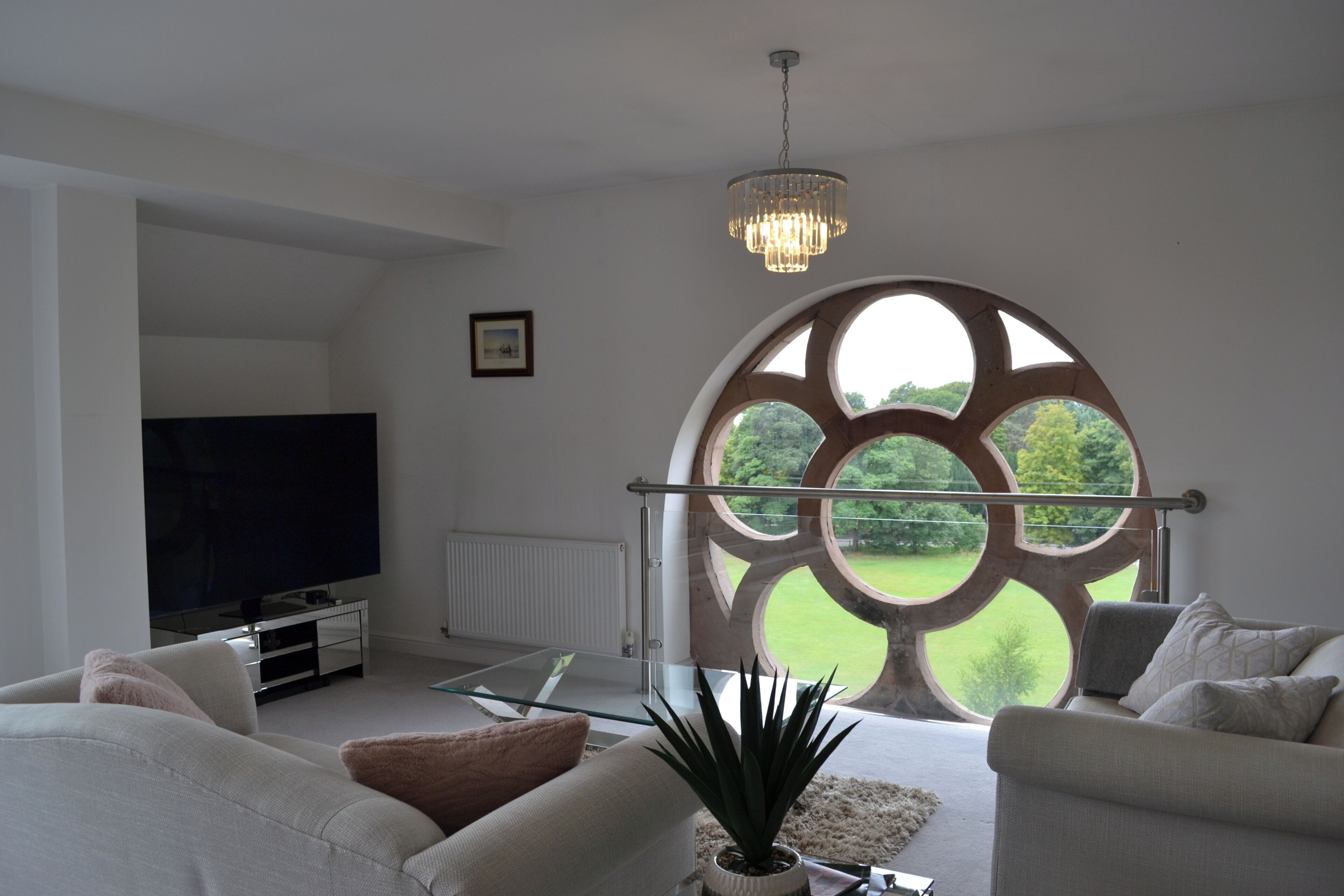 A modern living room with a large window, a flat-screen TV, and a chandelier.